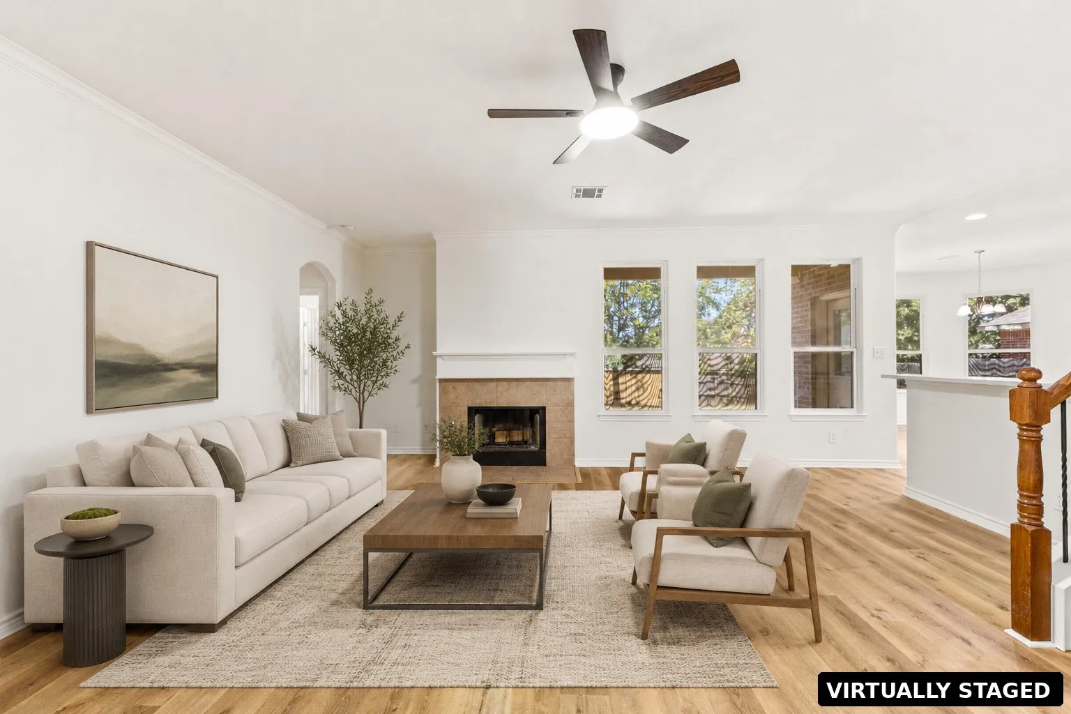 Wood-finish flooring, crown molding, a tiled fireplace, multiple windows, and a ceiling fan with integrated lighting