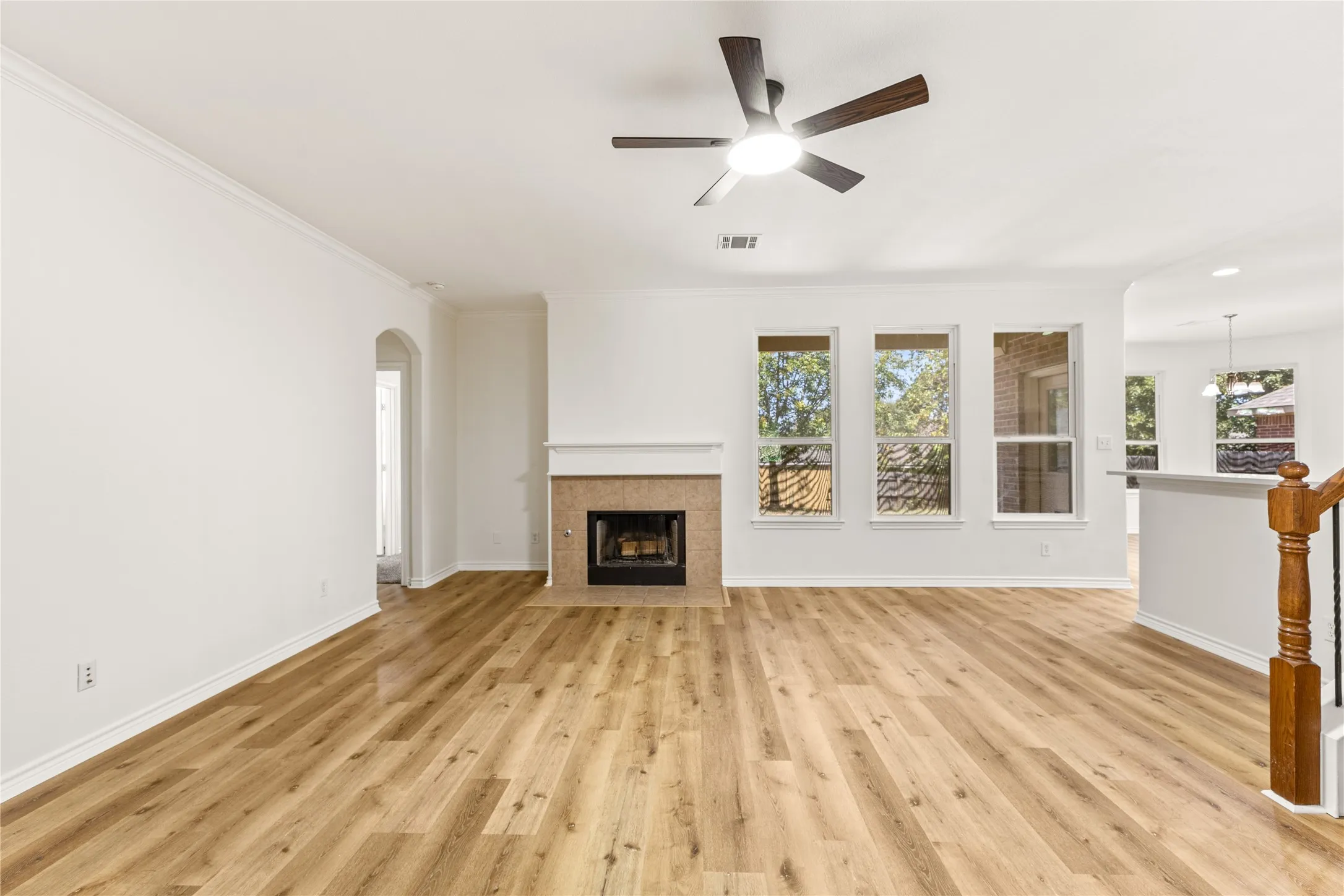 Expansive living area featuring light wood-finish flooring, a contemporary ceiling fan, and a fireplace with a stone-finish surround