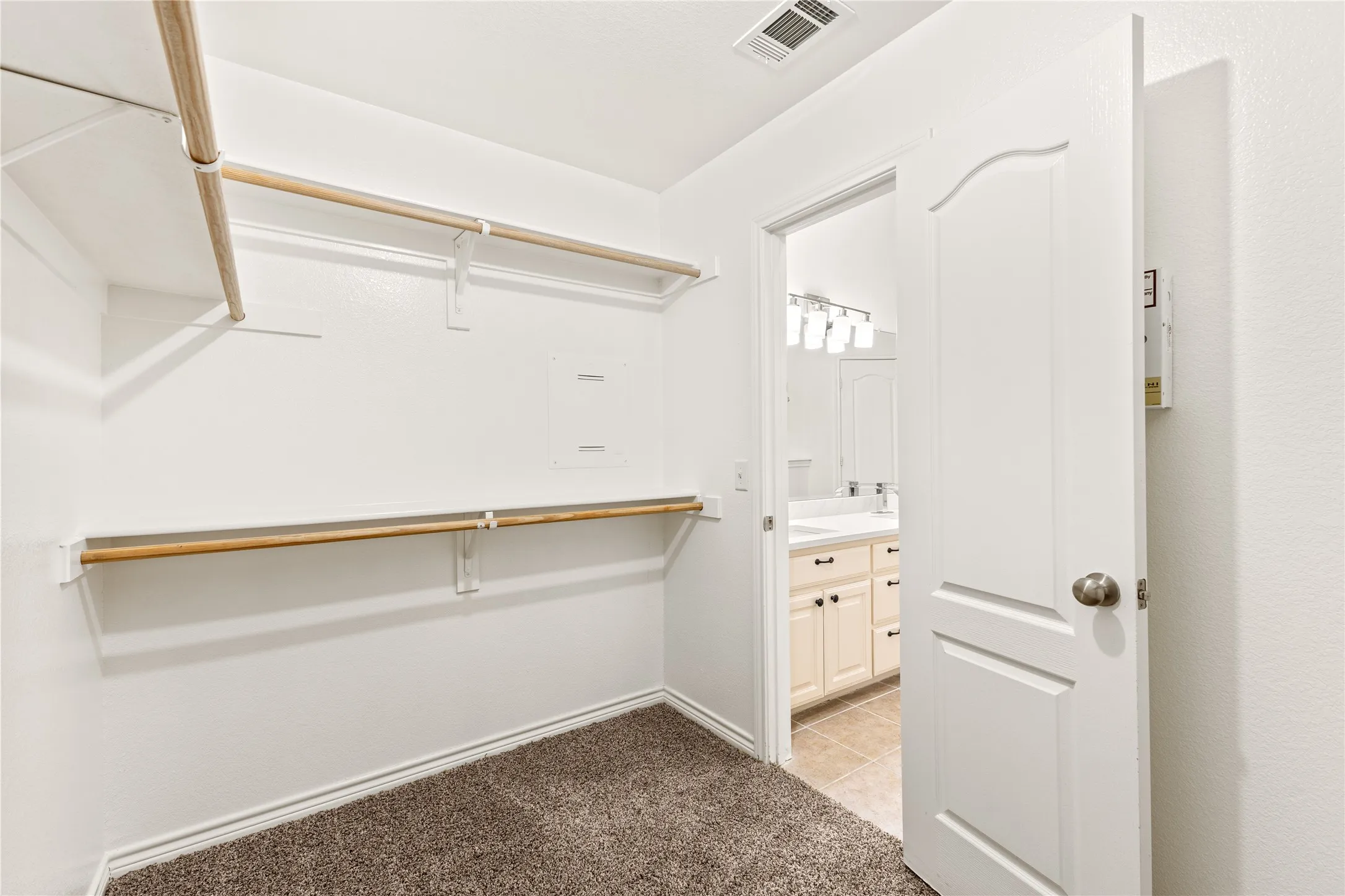 White walls with two levels of clothing rods, carpeted flooring, and a six-panel interior door