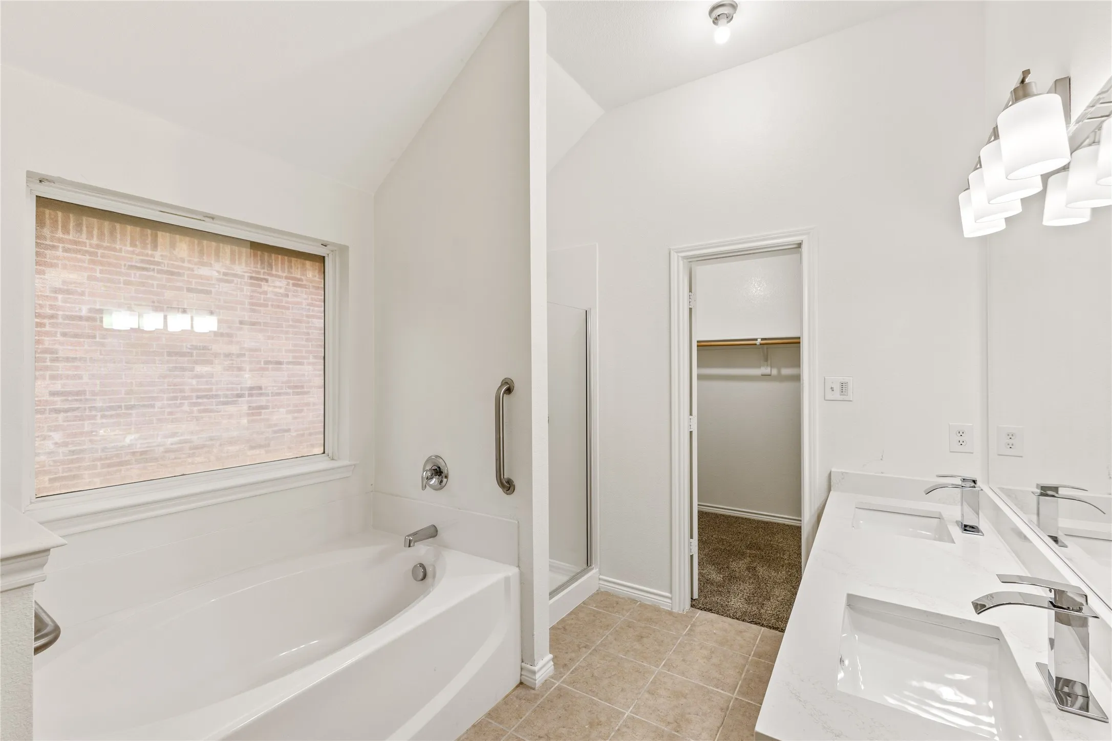 Vaulted ceiling, dual vanity with undermount sinks, chrome fixtures, built-in bathtub, and walk-in shower
