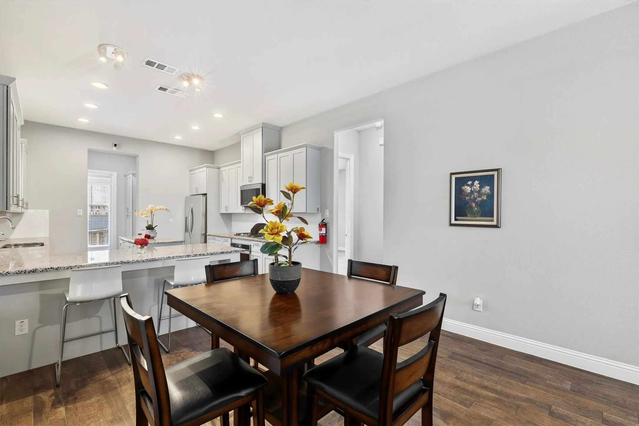 Open-concept kitchen and dining area featuring light-toned cabinetry, stainless steel appliances, and a breakfast bar with stone-finish countertops