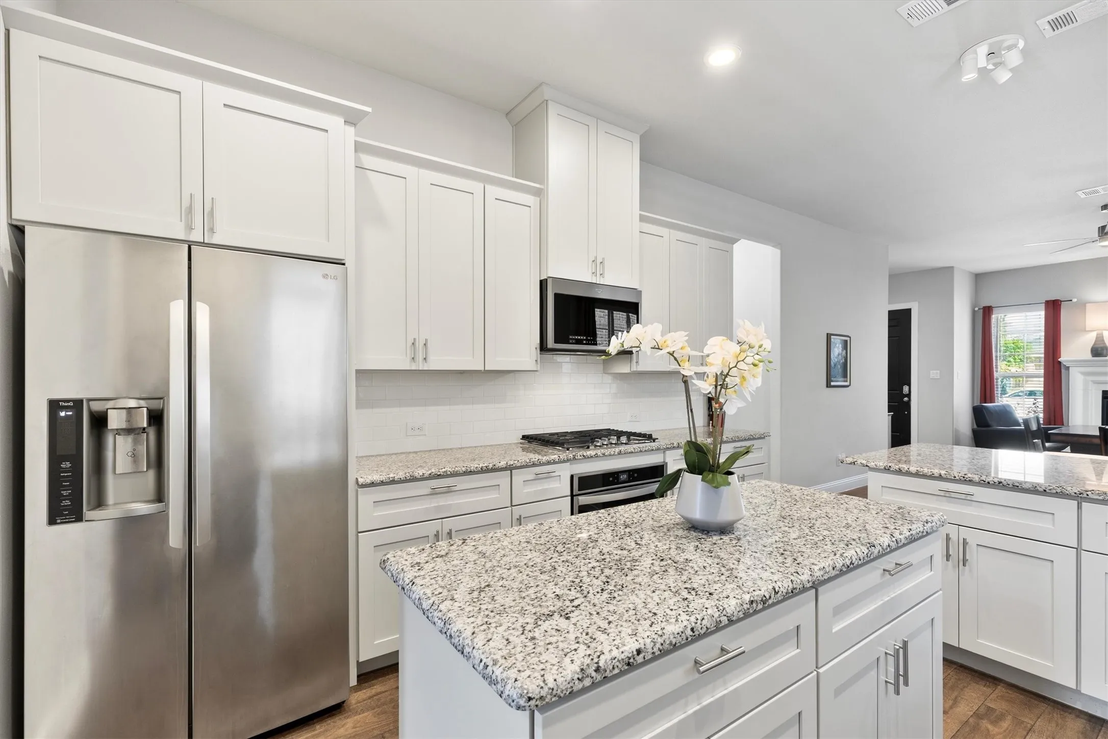 Kitchen featuring white cabinetry, stainless steel appliances, speckled stone countertops, a tile backsplash, and wood-finish flooring