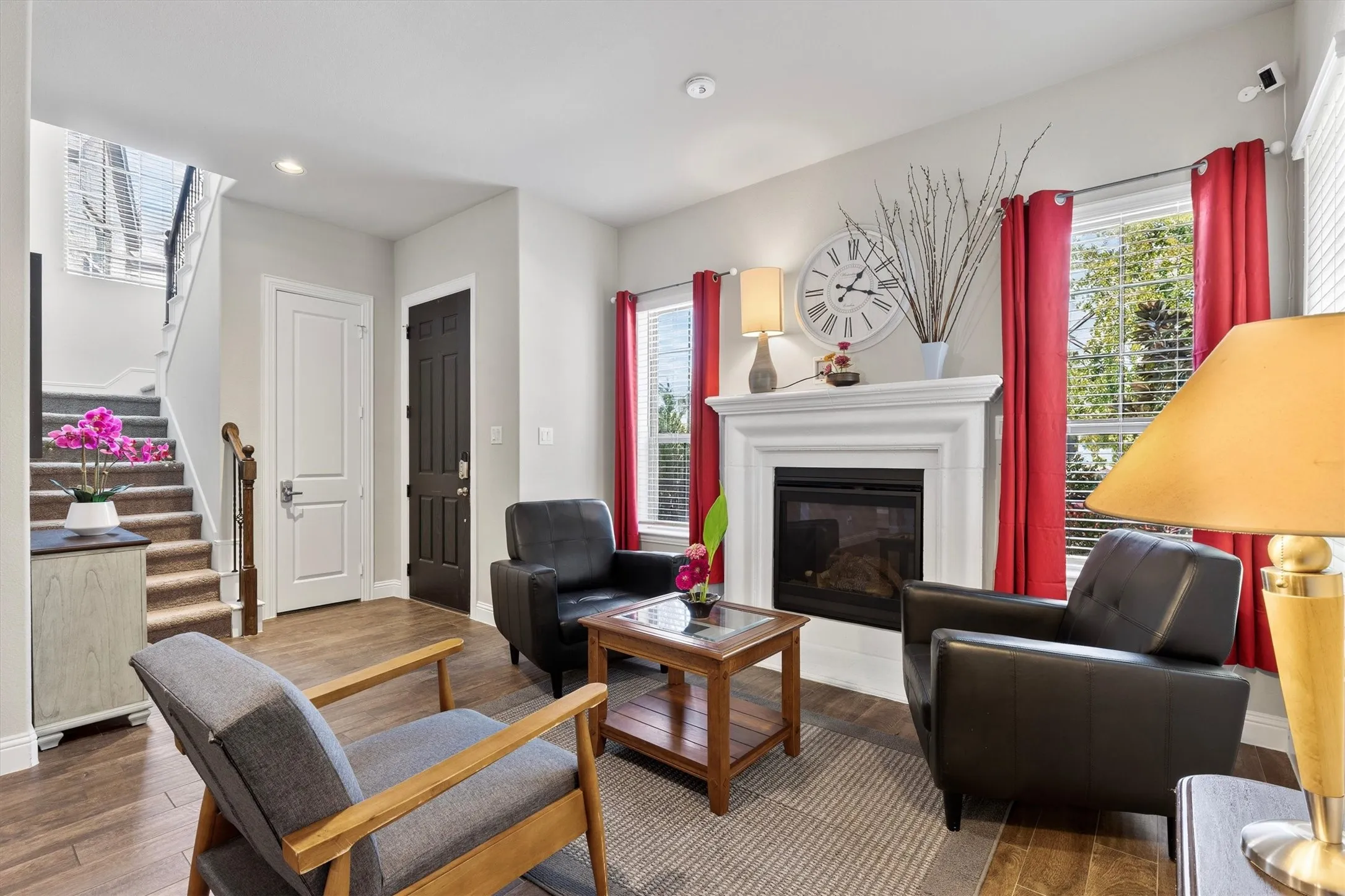 Living area featuring a fireplace with a white mantel, wood-finish flooring, and a staircase with wood handrails