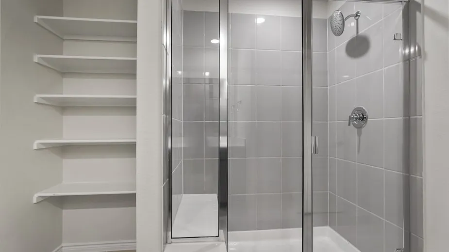 Glass-enclosed shower with ceramic tile surround, chrome fixtures, and built-in shelving