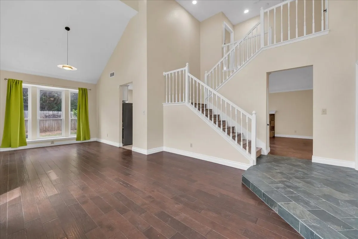 Vaulted ceiling, wood-finish flooring, staircase with white balusters, recessed lighting, and a bay window