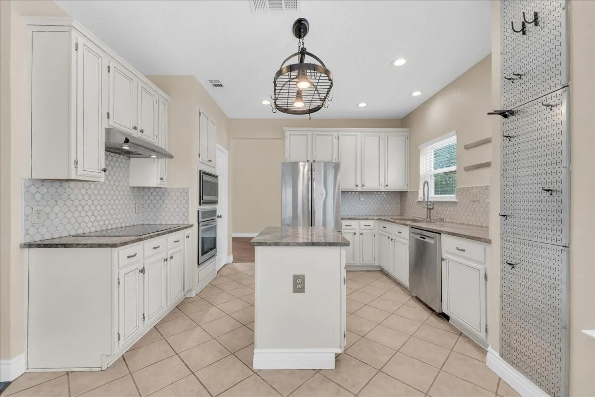 Kitchen featuring white cabinetry, stainless steel appliances, a center island with countertop, tiled flooring, and a decorative light fixture