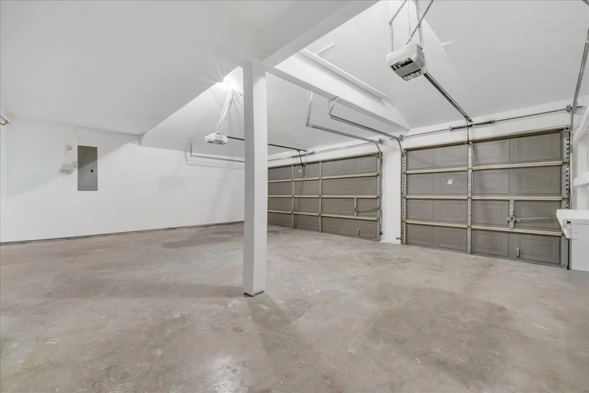 Two overhead garage doors, concrete flooring, exposed ceiling beams, and overhead lighting