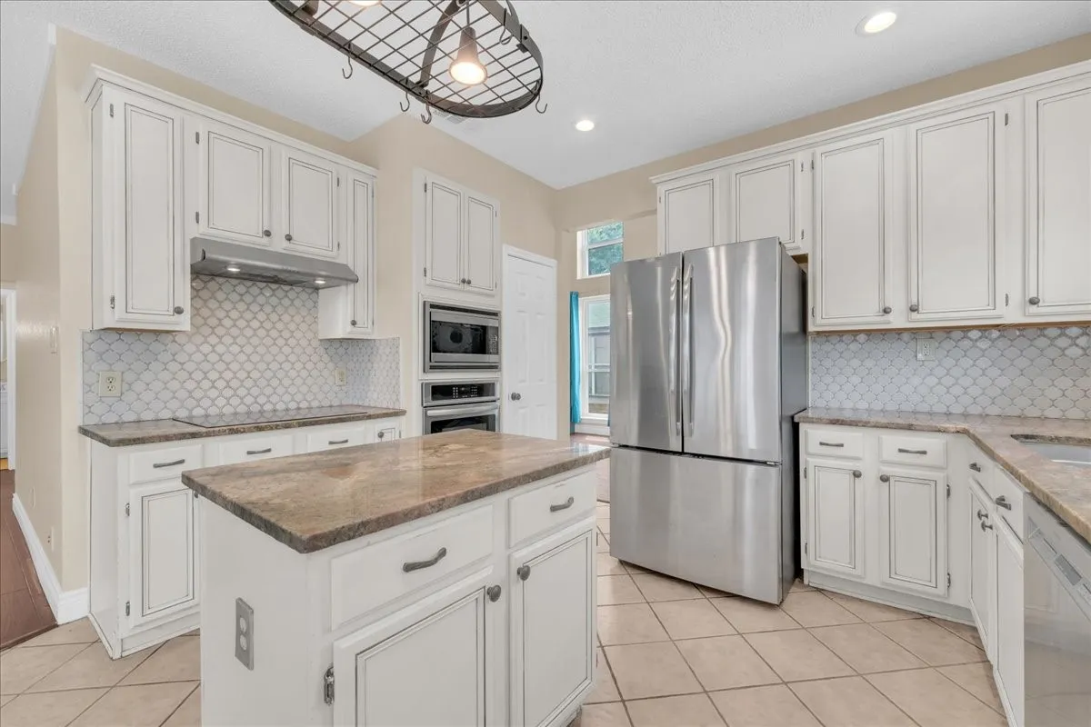 White cabinetry, a center island with countertop, a tile backsplash, stainless steel appliances, and tile flooring