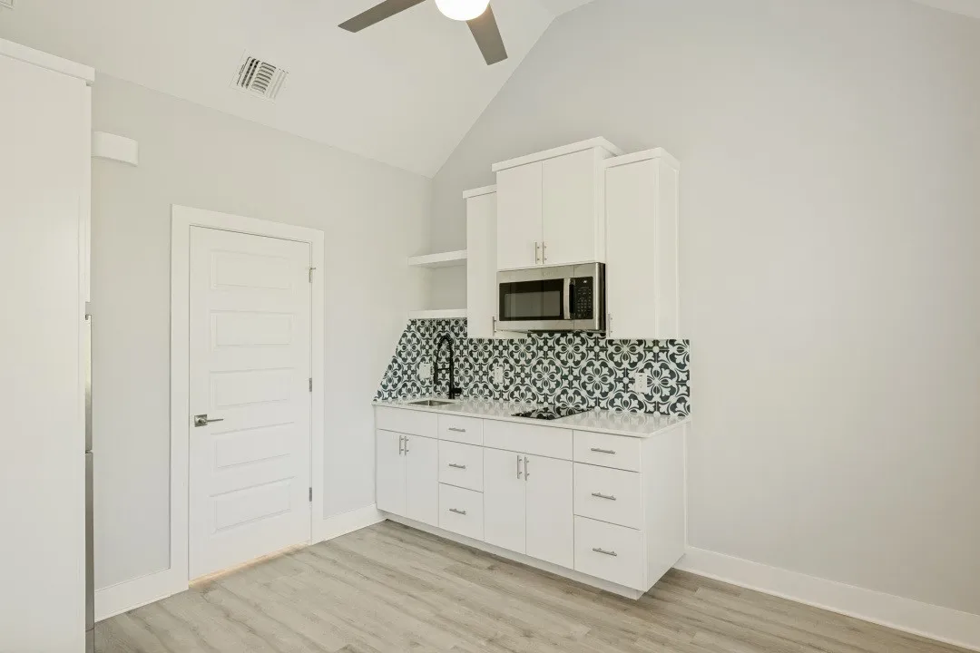 Vaulted ceiling with a ceiling fan, white paneled door, wood-finish flooring, built-in microwave, and patterned tile backsplash