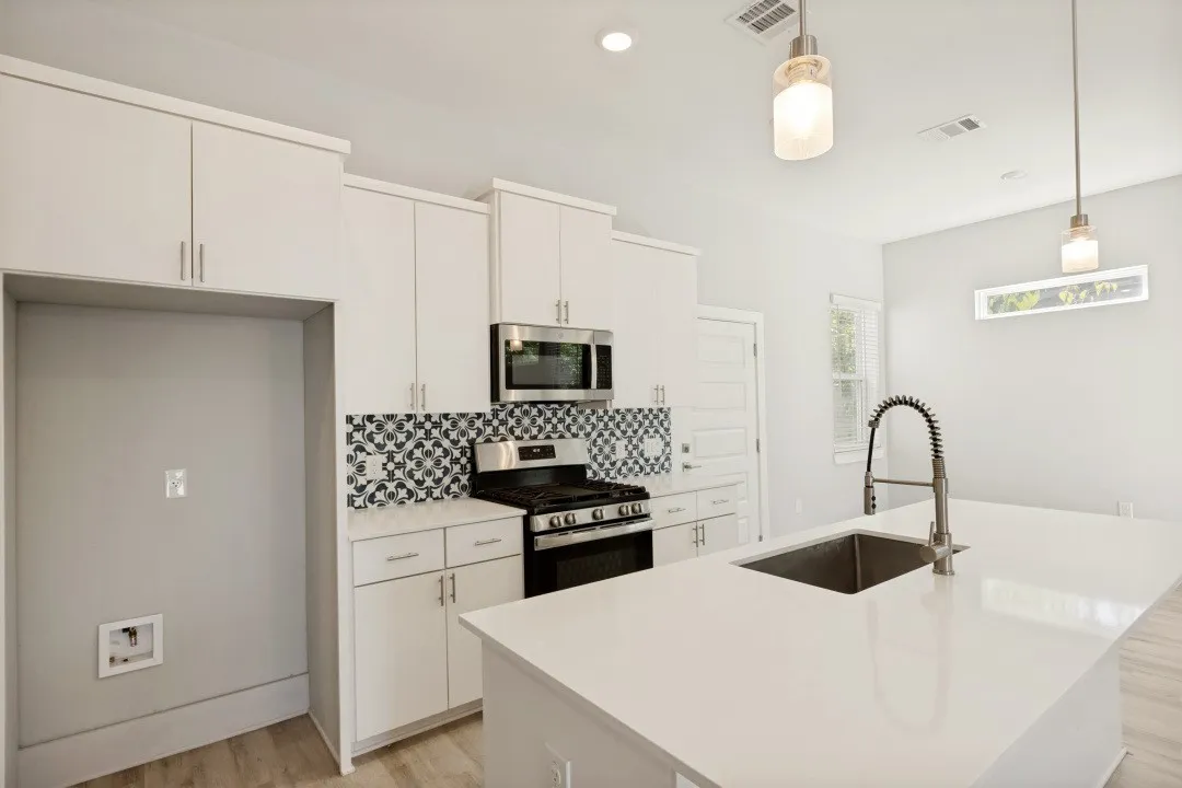 Modern kitchen featuring white cabinetry, stainless steel appliances, a patterned tile backsplash, a large island with an undermount sink, and wood-finish flooring