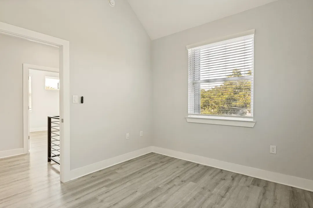 Vaulted ceiling, wood-finish flooring, white trim, and a window with blinds