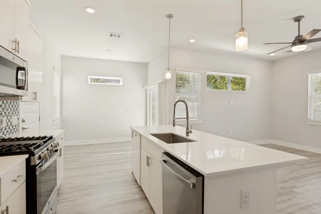 Modern kitchen featuring white cabinetry, stainless steel appliances, a center island with sink, pendant lighting, and wood-finish flooring