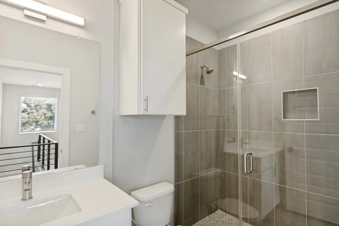 Bathroom featuring a frameless glass shower enclosure, a tiled shower surround with a built-in niche, and a white vanity with an integrated sink