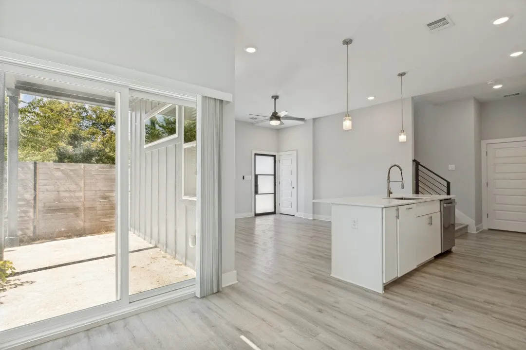 Open-concept living area featuring wood-finish flooring, recessed lighting, a kitchen island with an undermount sink and stainless steel dishwasher, and sliding glass doors opening to a private patio