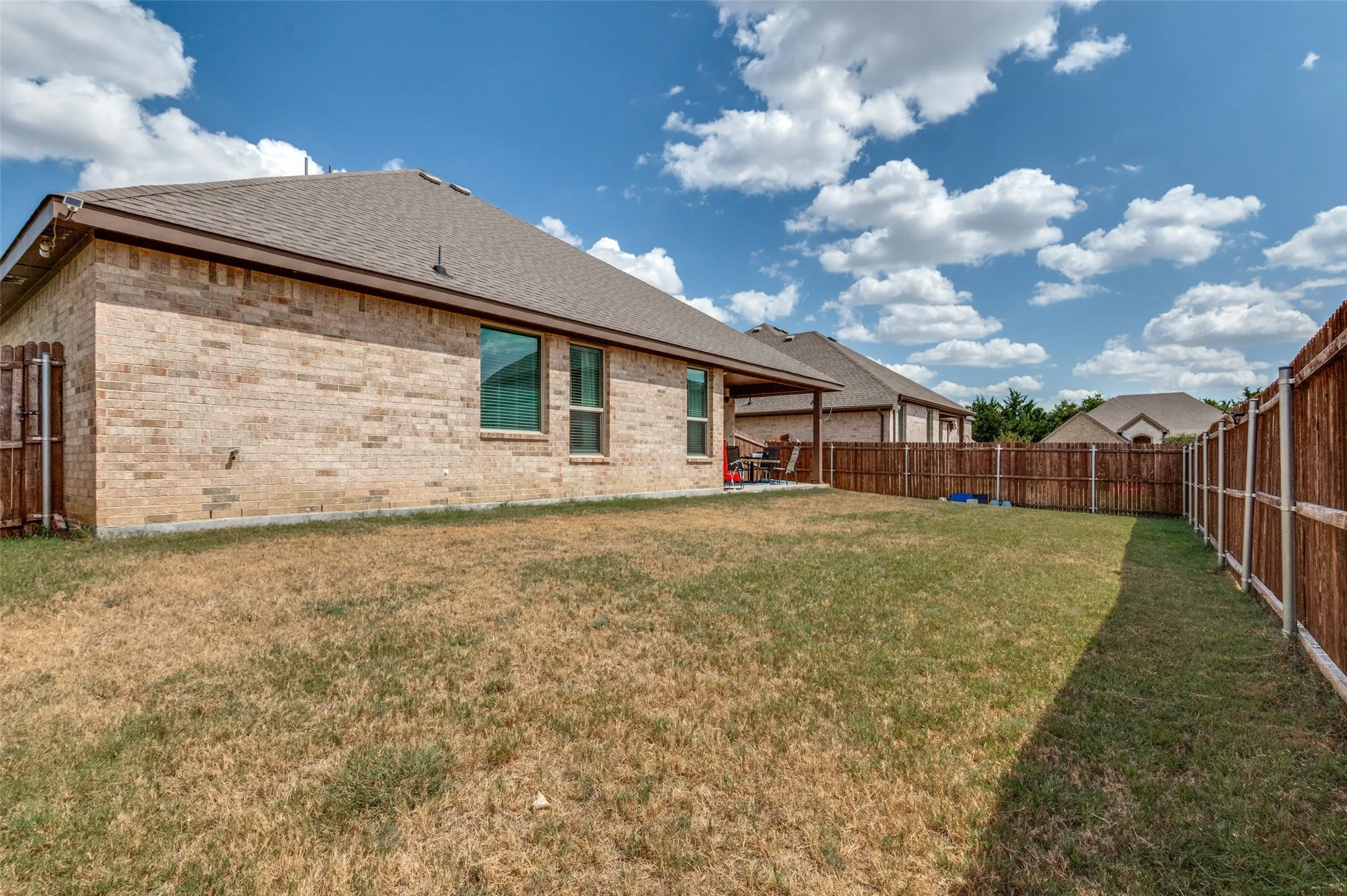 Expansive backyard with a full privacy fence, brick exterior, and covered patio