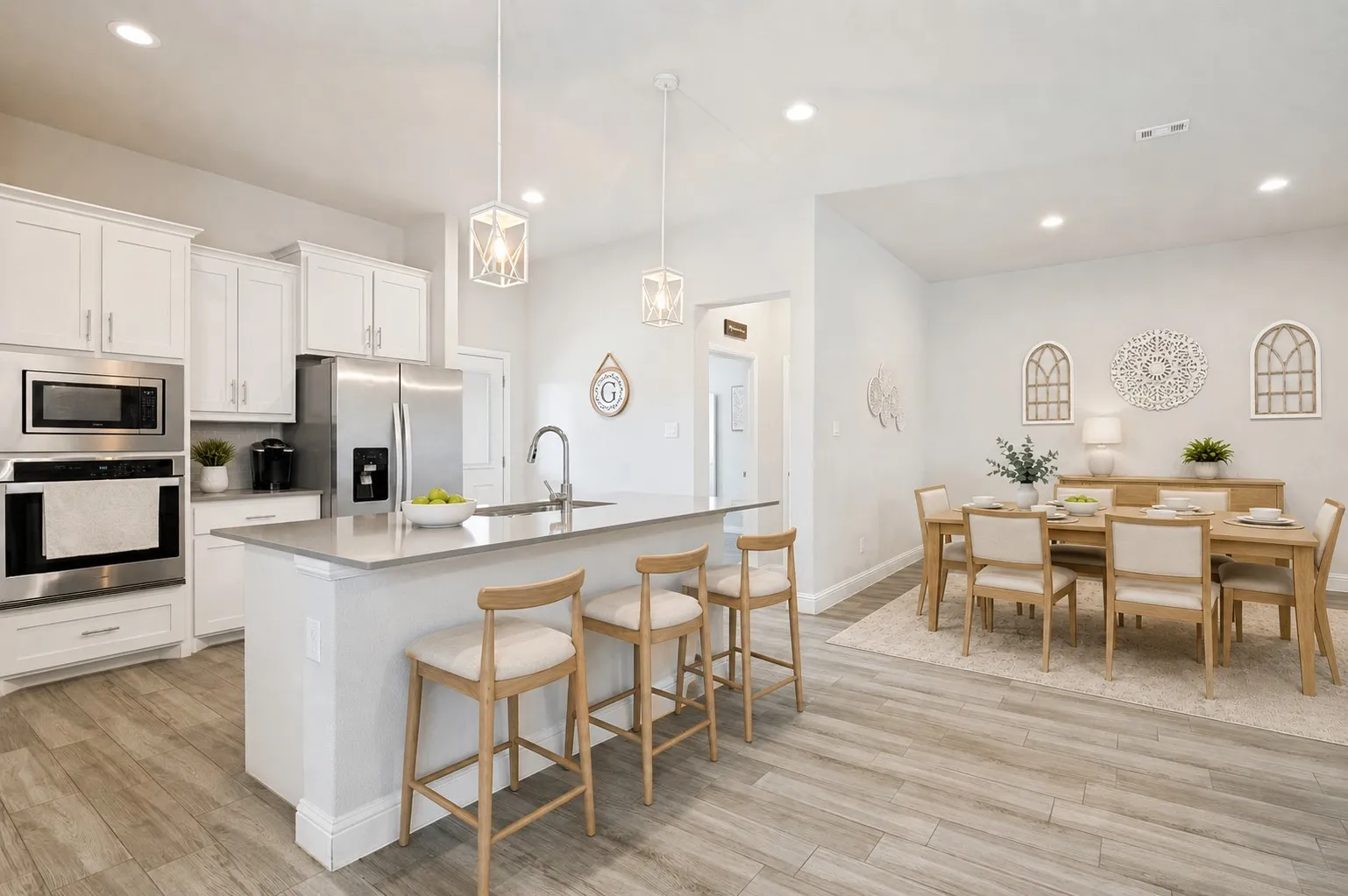 **Virtually staged for effect**Kitchen island with an undermount sink, stainless steel appliances, white cabinetry, and wood-finish flooring extending into the dining area