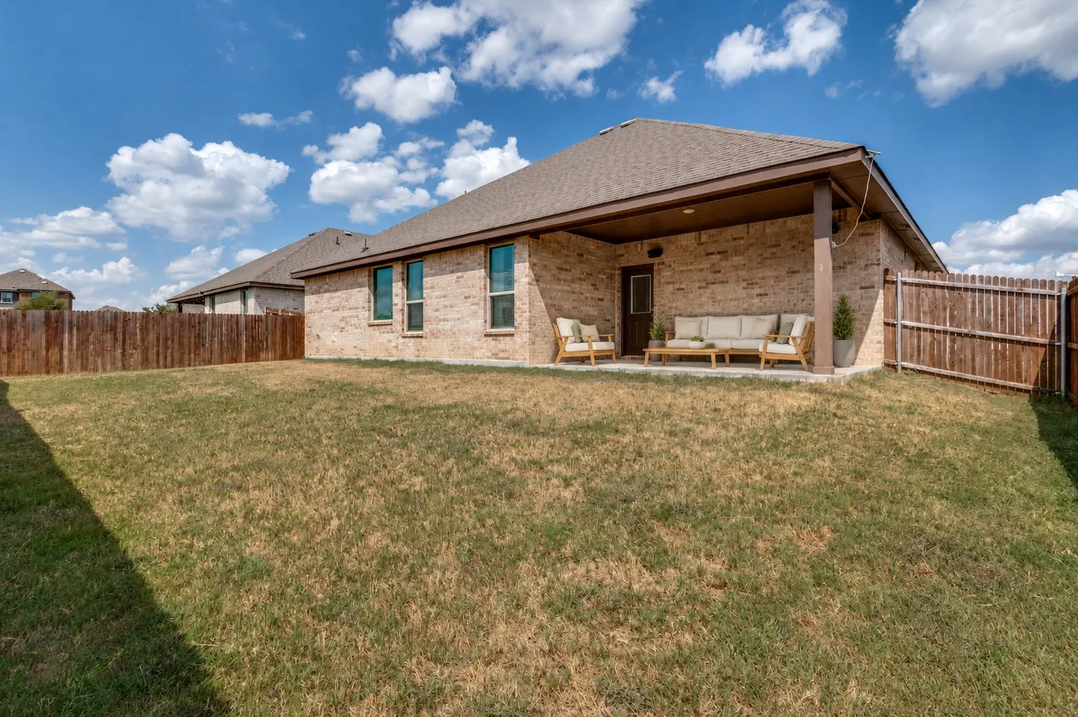 **Virtually staged for effect**Expansive backyard featuring a covered patio, brick exterior, and a privacy fence