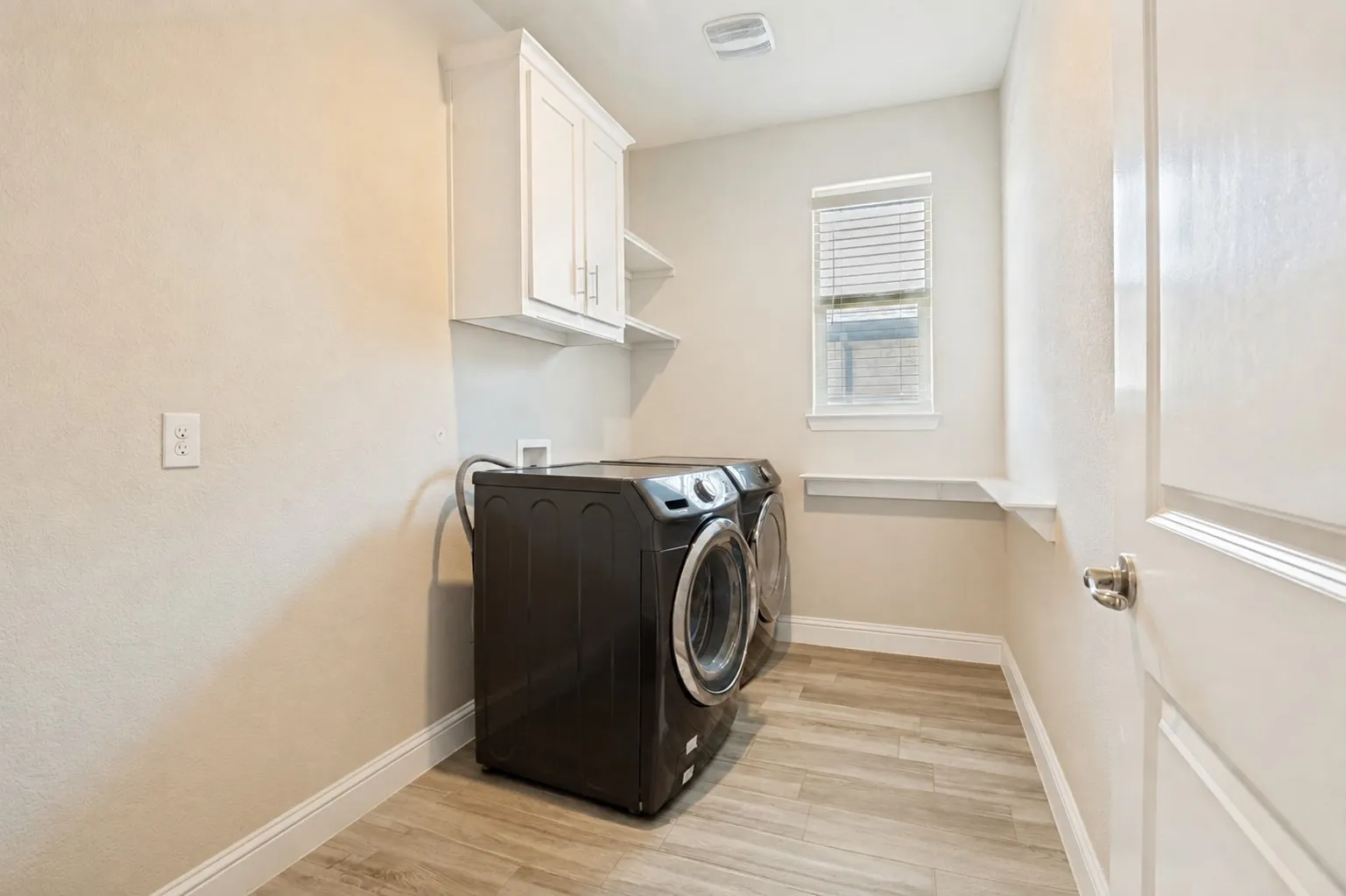 **Virtually staged for effect**Laundry area featuring wood-finish flooring, built-in shelving, white cabinetry, and a window with blinds