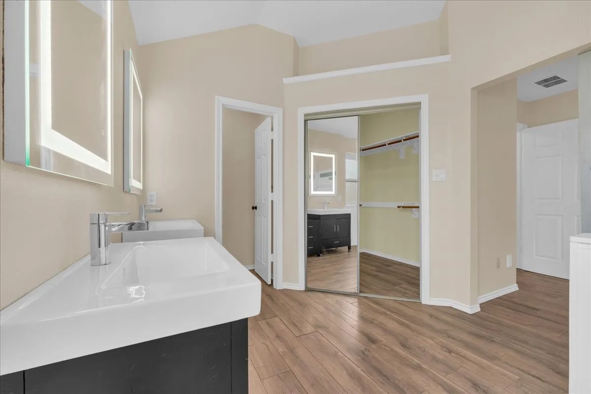Dual vanity with integrated sinks, illuminated mirrors, wood-finish flooring, and a mirrored closet