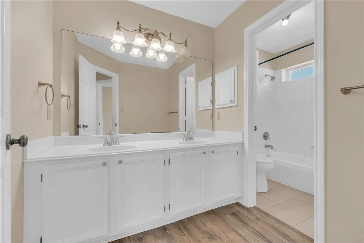 Dual vanity with white cabinetry, wood-finish flooring, and a built-in tub with shower