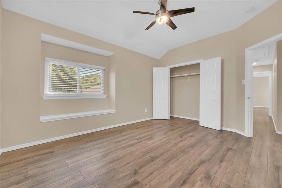 Vaulted ceiling with a ceiling fan, wood-finish flooring, recessed window, and double-door closet