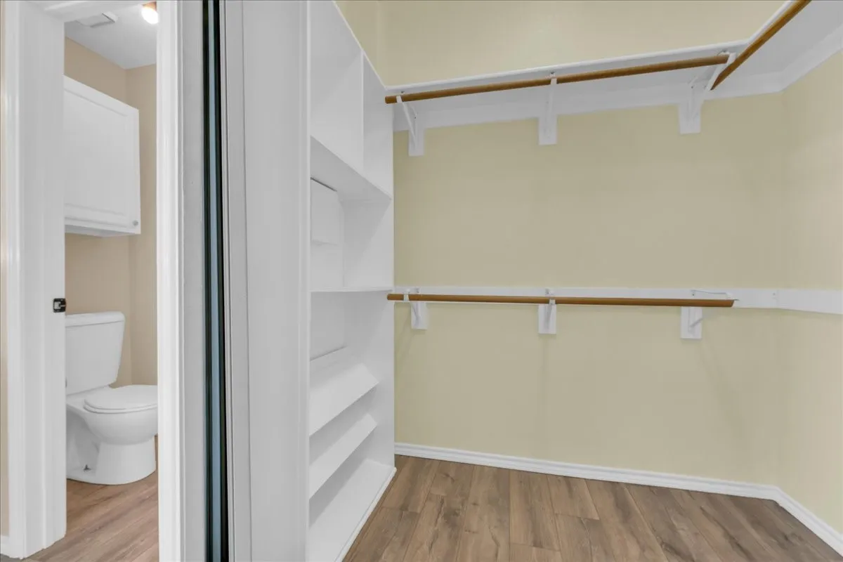 Walk-in closet featuring extensive built-in shelving, two clothing rods, and wood-finish flooring
