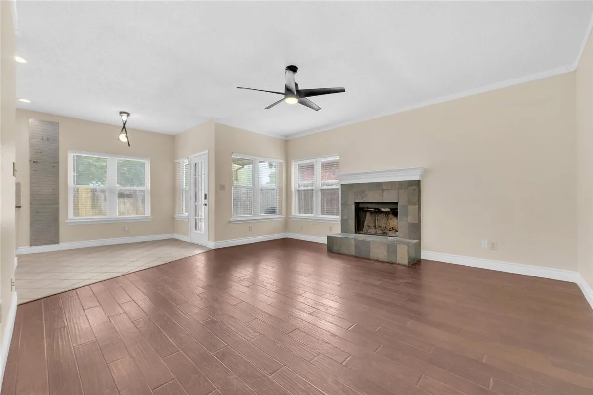 Wood-finish flooring, stone-clad fireplace with mantel, ceiling fan, recessed lighting, and multiple windows