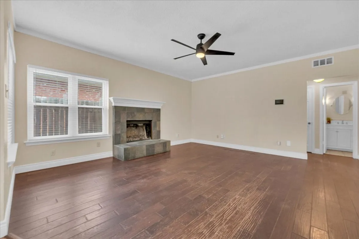 Spacious room featuring wood-finish flooring, a contemporary ceiling fan, and a fireplace with a stone-tile surround