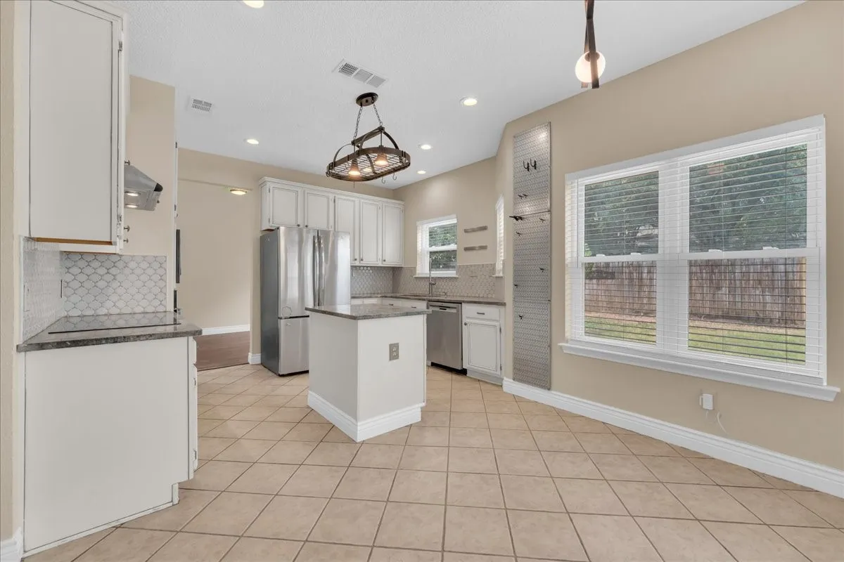 Kitchen featuring tile flooring, white cabinetry, a center island, stainless steel appliances, and a mosaic tile backsplash