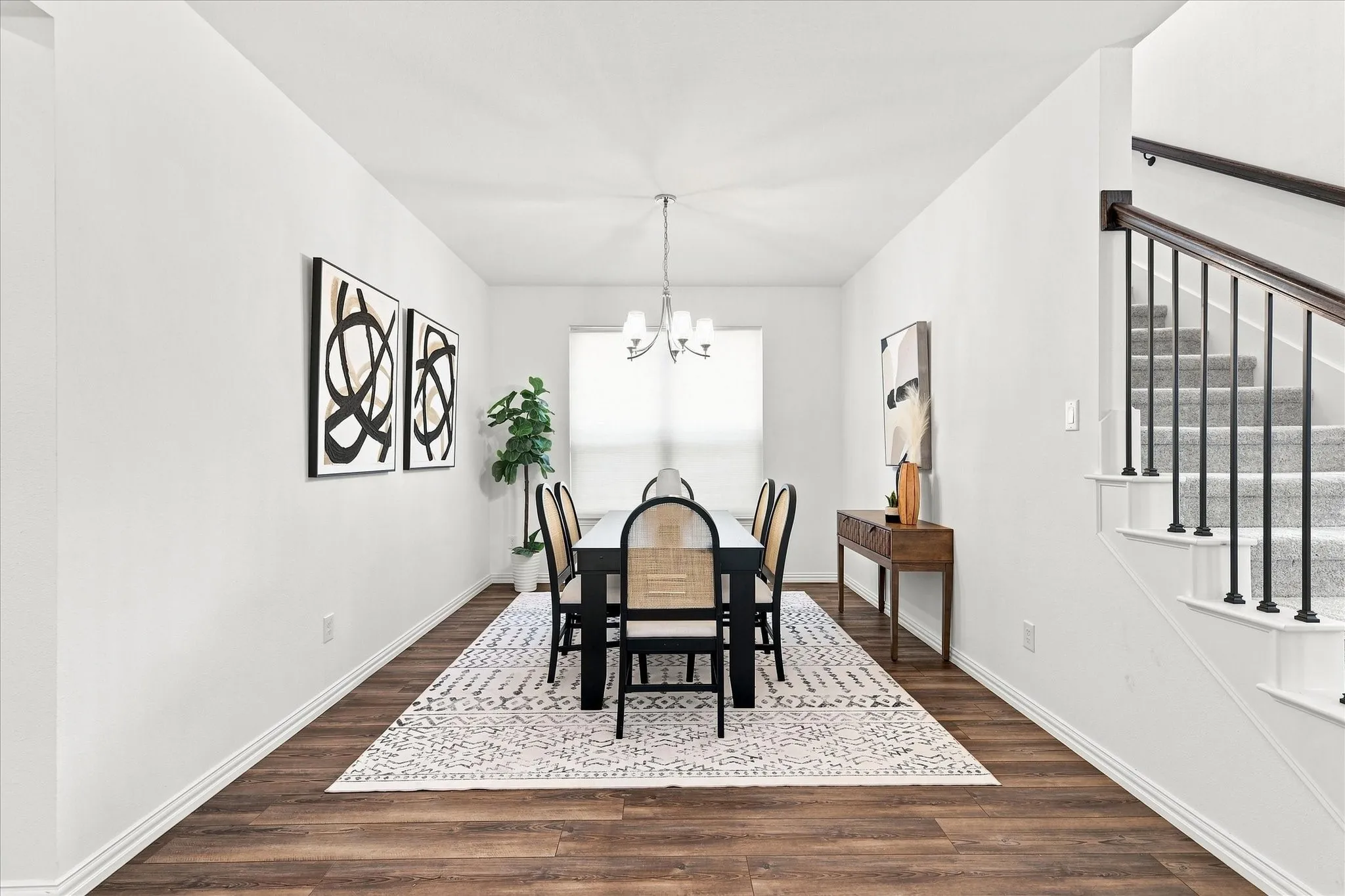 Wood-finish flooring, staircase with carpeted treads and wrought iron balusters, white wall finishes, and a chandelier lighting fixture