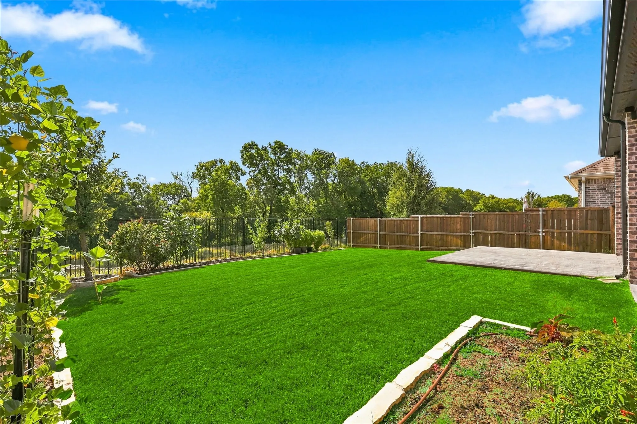 Expansive green lawn, concrete patio, wood privacy fencing, and a brick-sided exterior with gutters