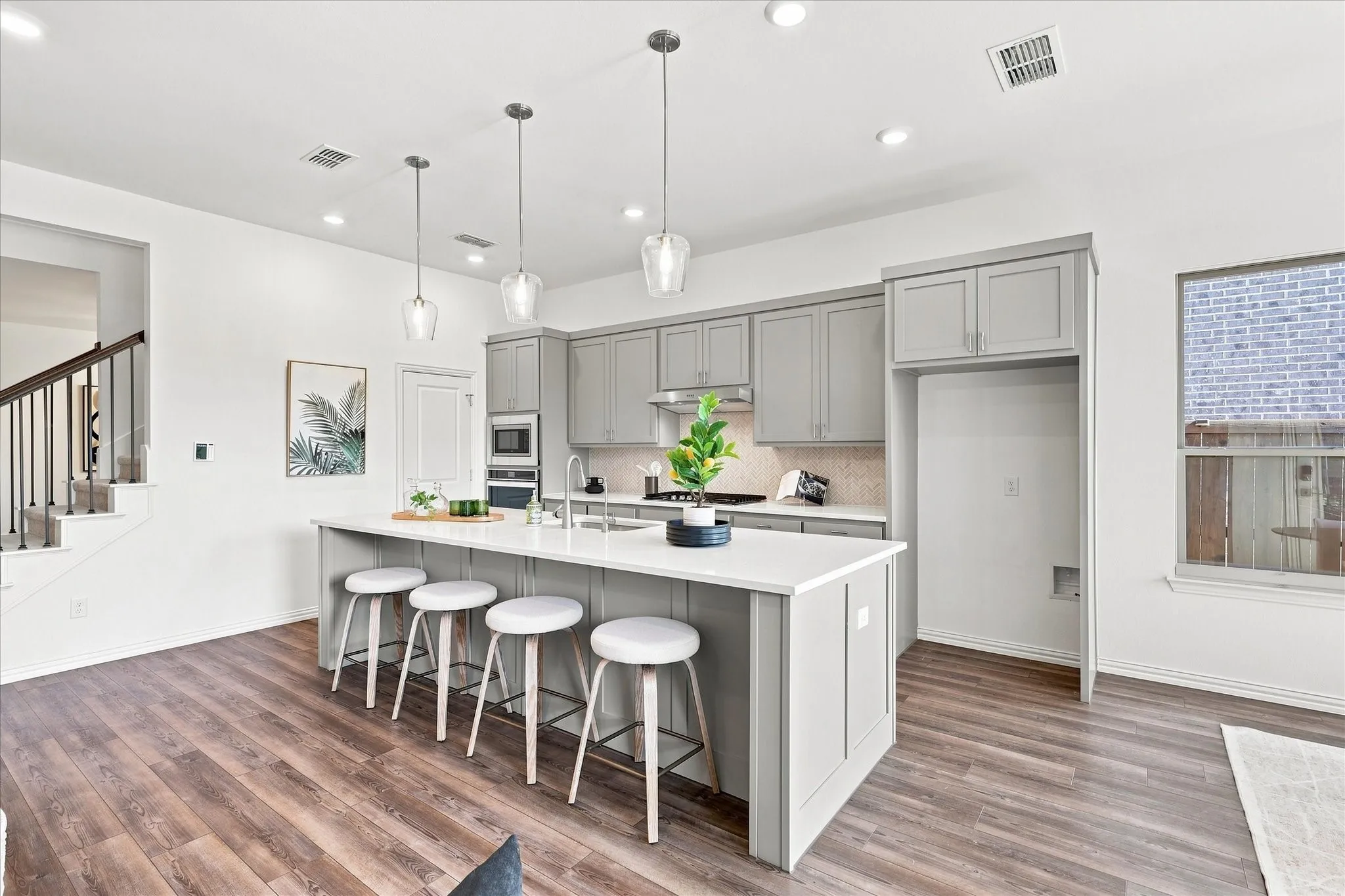 Kitchen featuring an island with seating, pendant lighting, built-in stainless steel appliances, wood-finish flooring, and white countertops