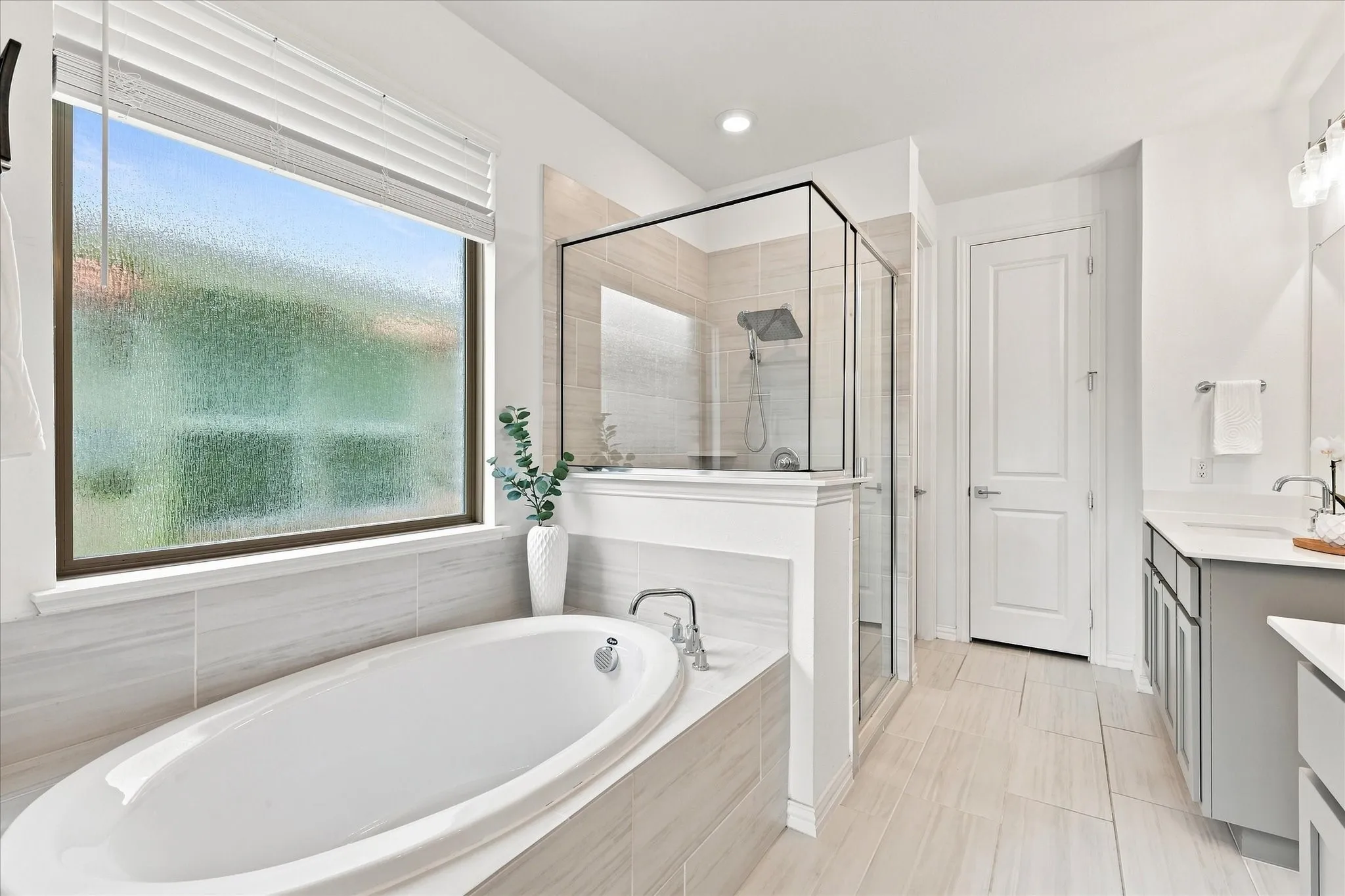 Soaking tub with surrounding tiled deck, glass-enclosed shower, dual vanity with undermount sinks, and tiled flooring