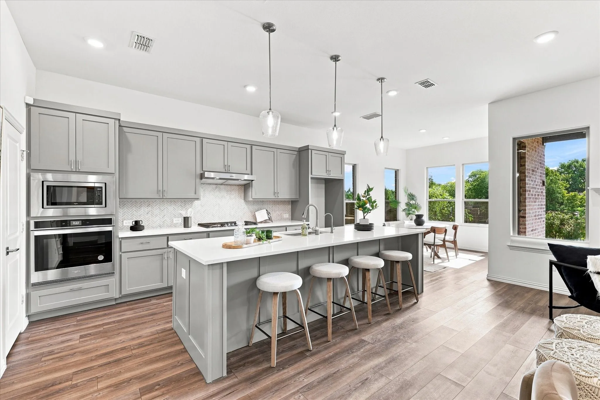 Open-concept kitchen featuring an oversized island, stainless steel appliances, grey shaker cabinetry, white countertops, and wood-finish flooring