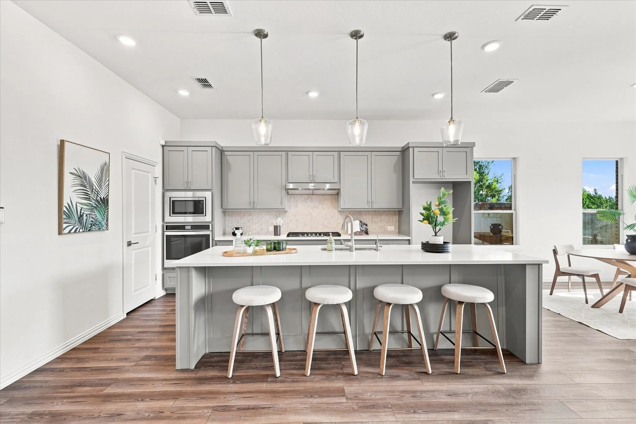 Modern kitchen featuring light gray cabinetry, built-in stainless steel appliances, a white island with pendant lighting, and wood-finish flooring