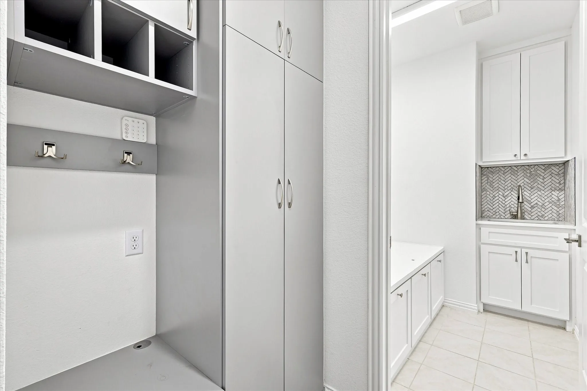 Built-in cabinetry with open shelving, hanging hooks, and a dedicated utility sink with a herringbone tile backsplash
