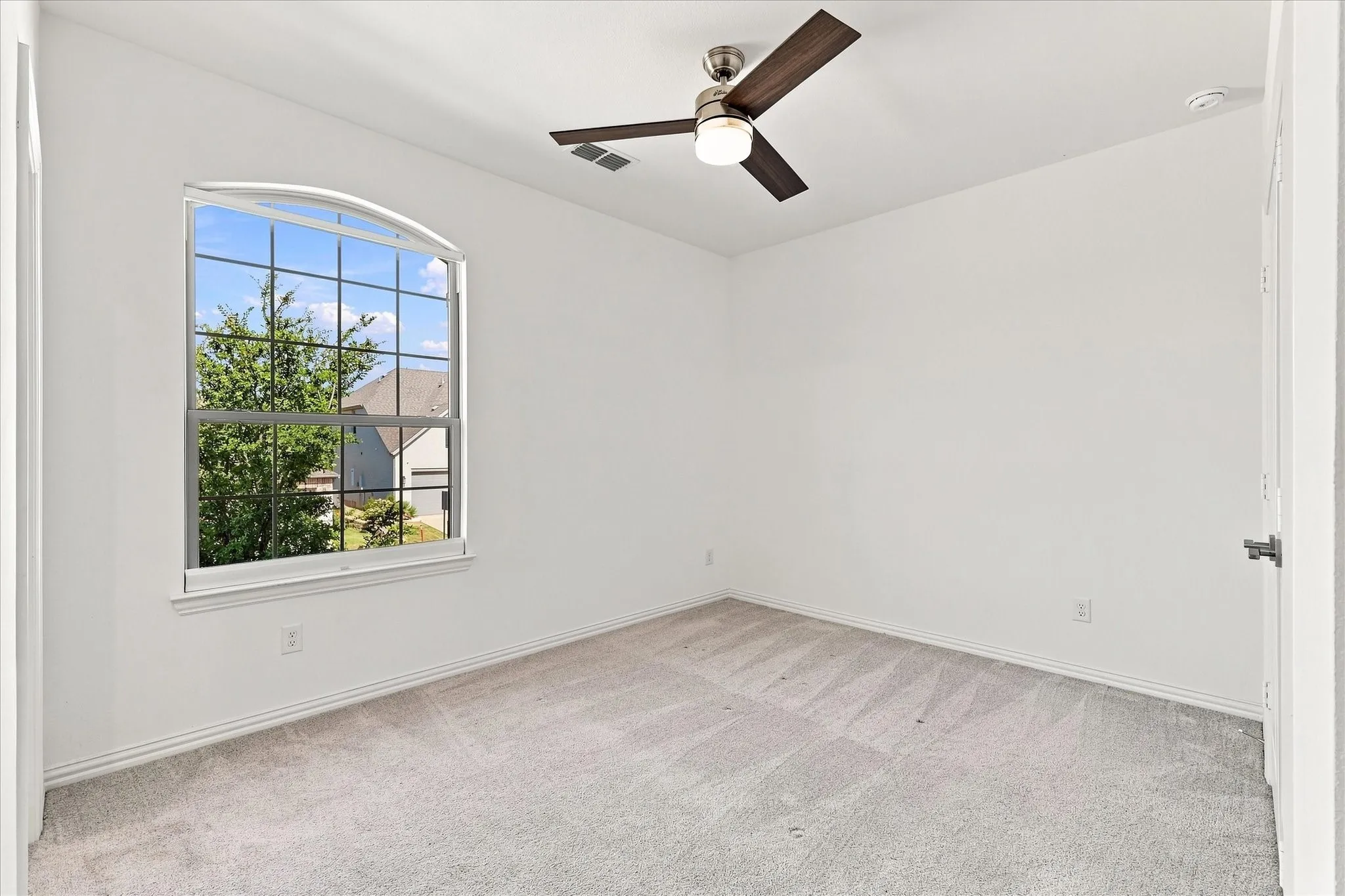 Arch-top window with grid pattern, neutral carpet, ceiling fan with light fixture, and white walls