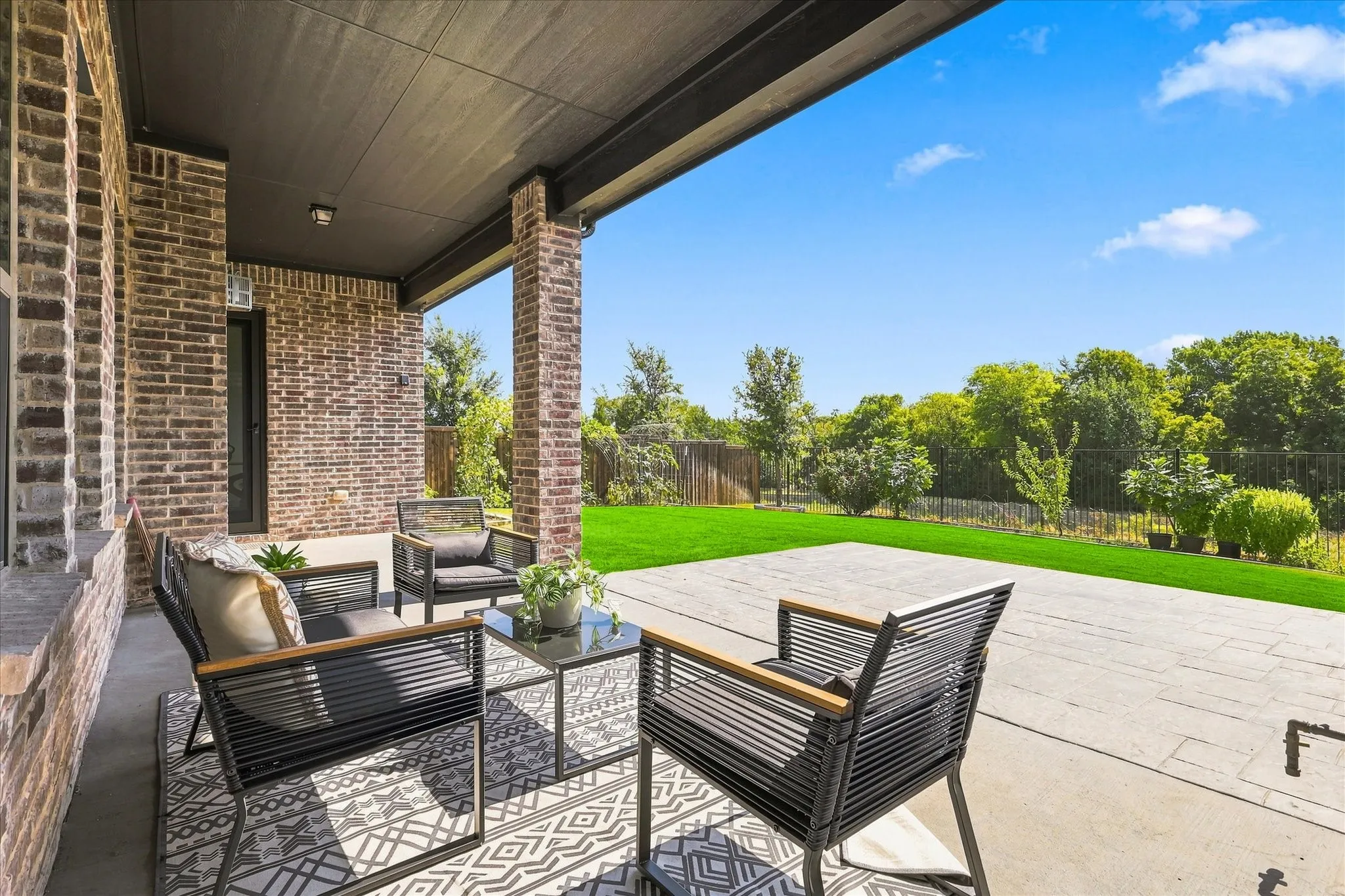 Covered patio with brick columns, recessed lighting, concrete flooring, and a manicured lawn beyond