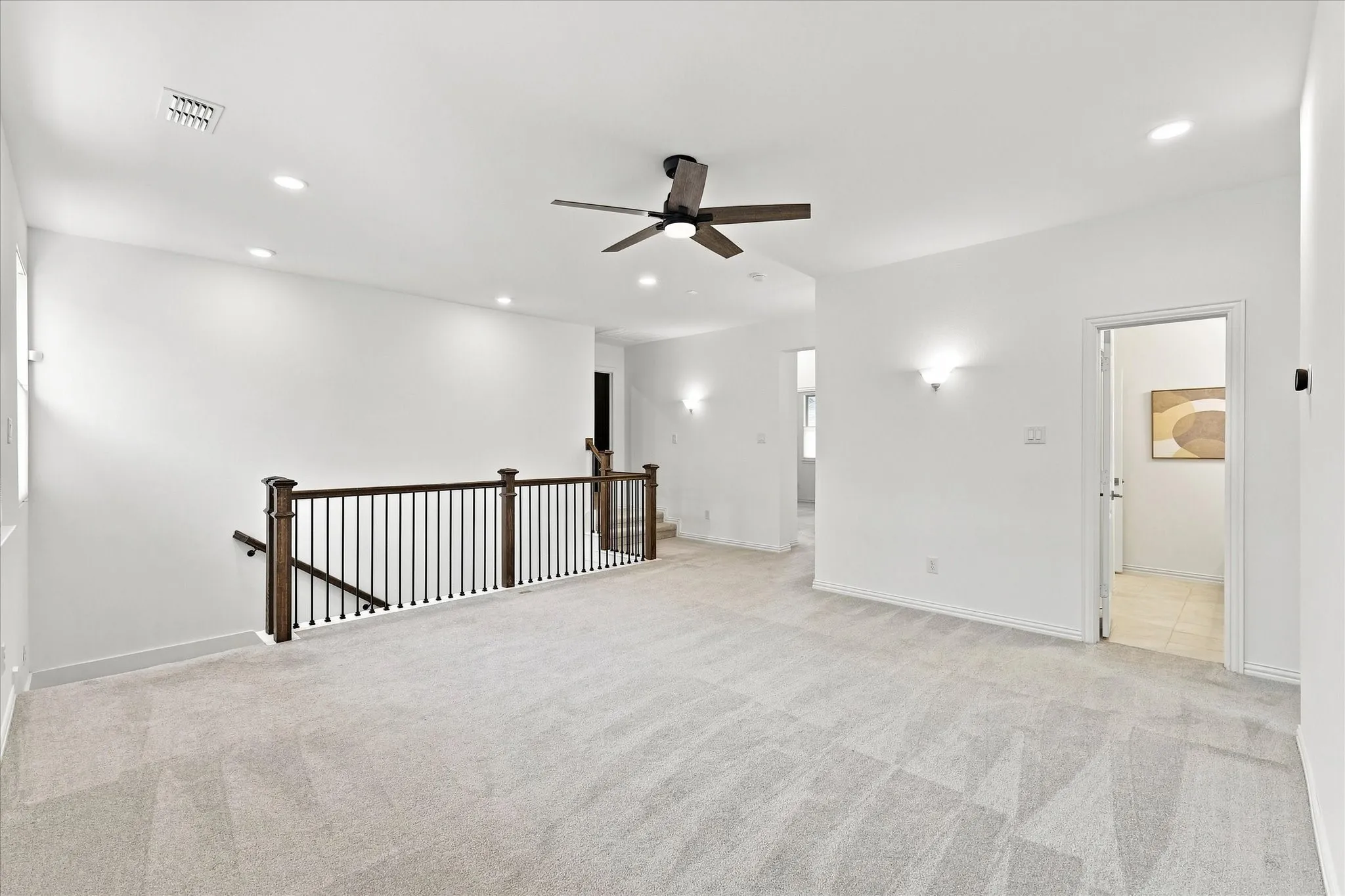 Expansive carpeted area featuring a ceiling fan, recessed lighting, and sconce light fixtures