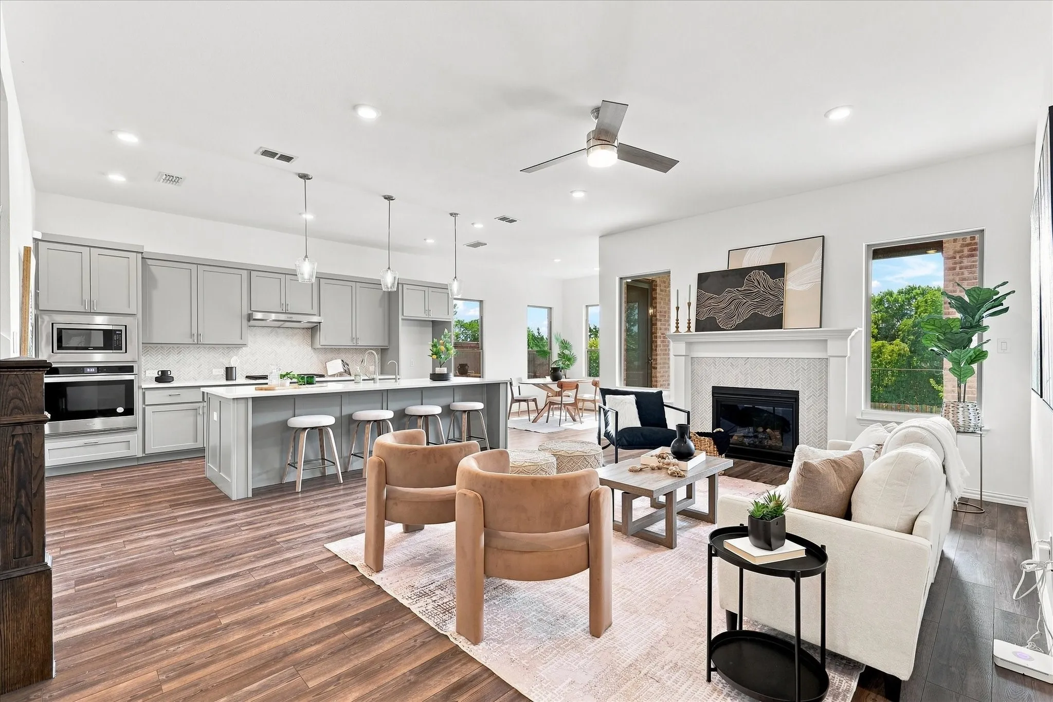 Open-concept living area featuring wood-finish flooring, a kitchen island with pendant lighting, integrated stainless steel appliances, a fireplace with a mantel, and a ceiling fan