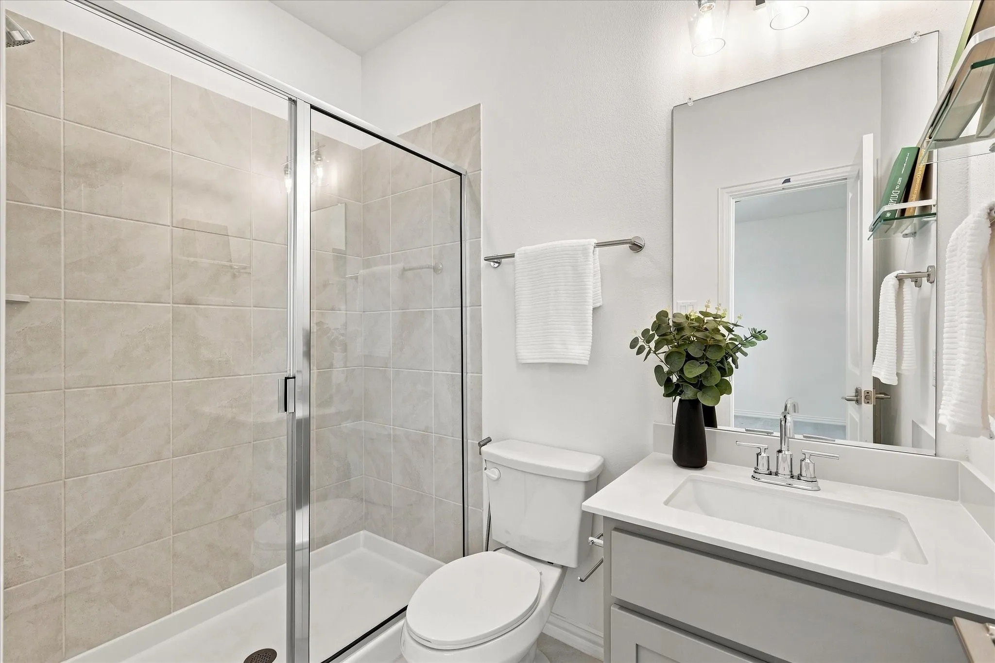 Glass-enclosed shower with tile surround, single vanity with integrated sink, chrome faucet, and expansive wall mirror
