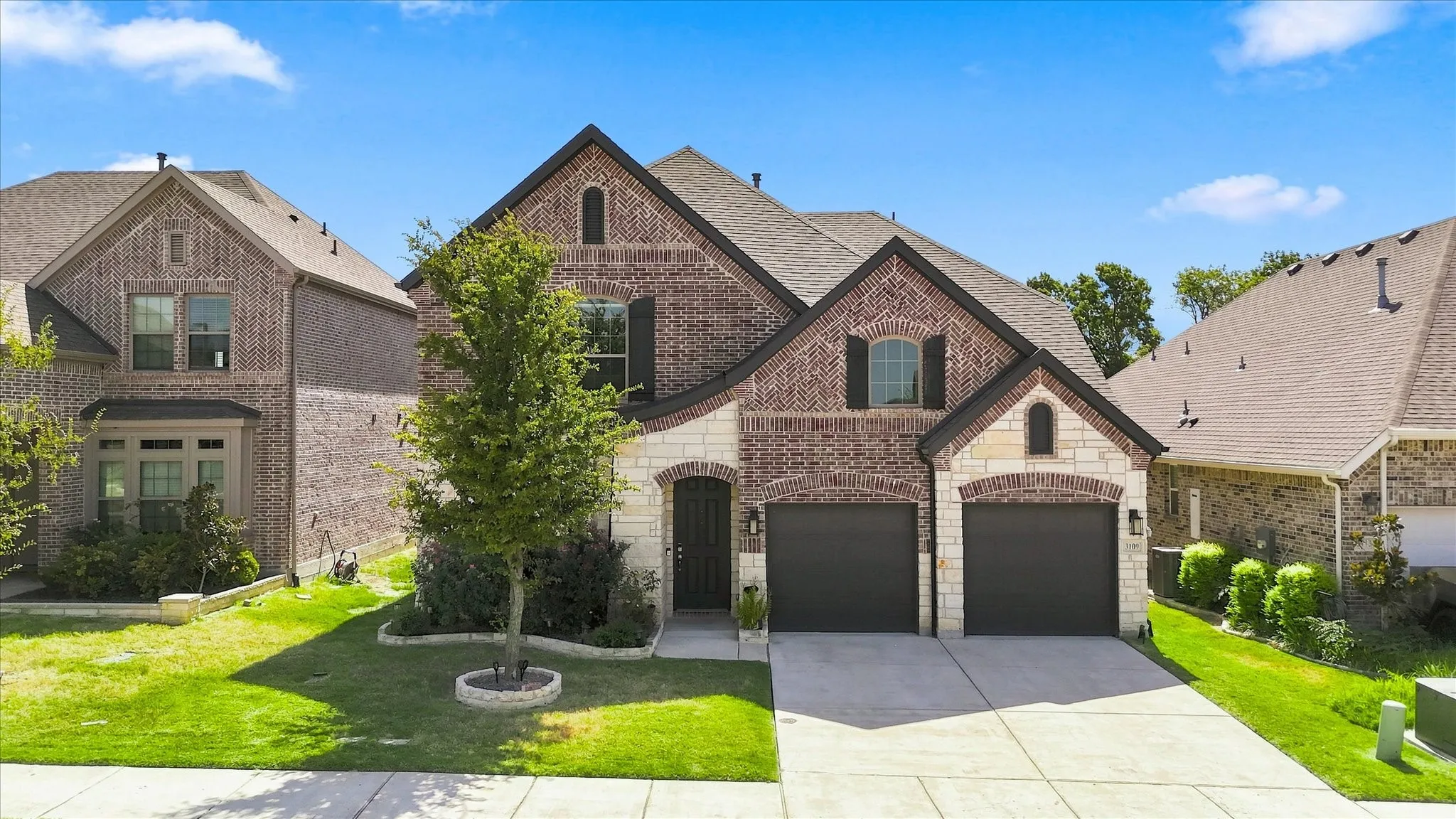 Brick and stone facade with dark shutters, dual garage doors, arched entryway, and established landscaping