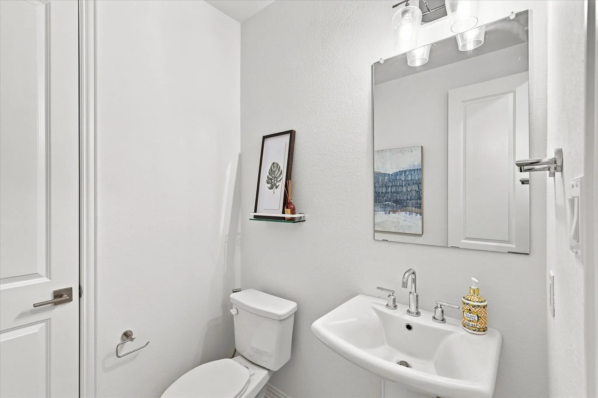 Pedestal sink with chrome fixtures, large wall mirror, and modern overhead lighting