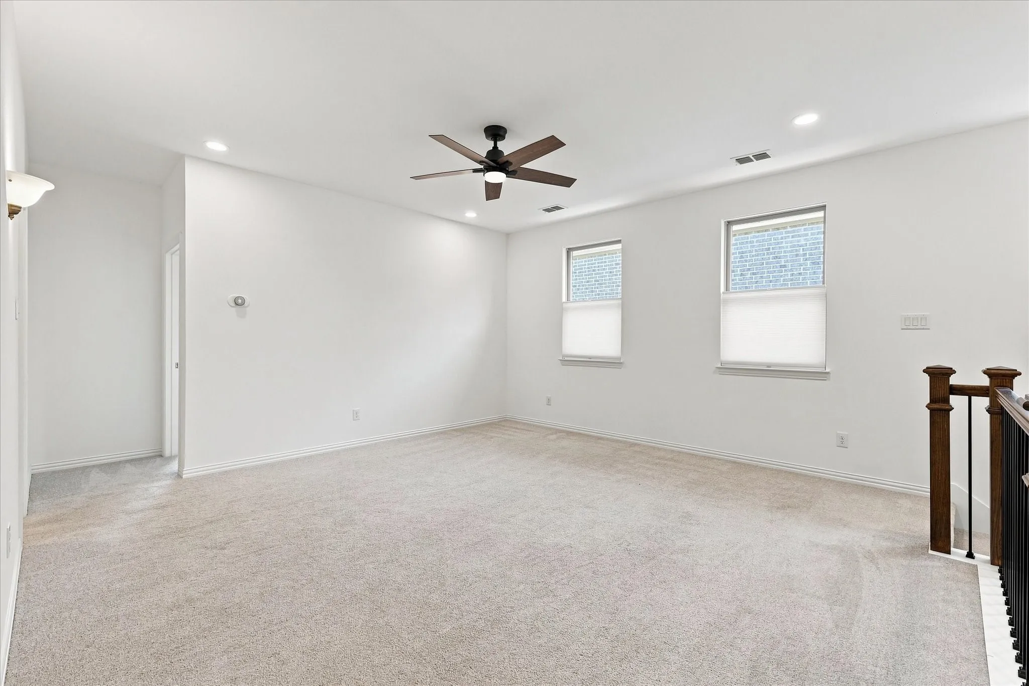 Carpeted room with recessed lighting, a ceiling fan, two windows, and a wood and metal railing