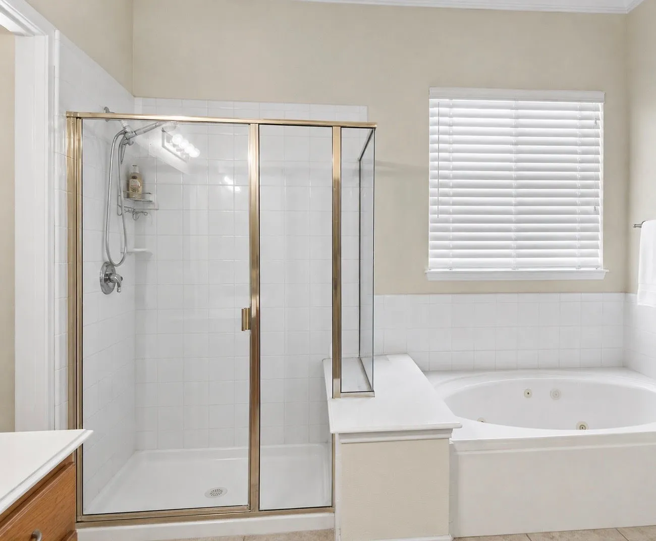 Glass-enclosed shower with a brushed brass frame, white tiled shower surround, recessed shower niche, and an integrated jetted soaking tub