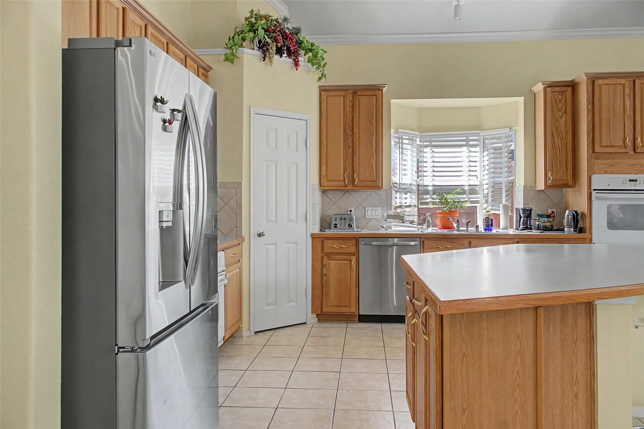 Kitchen featuring wood cabinetry, stainless steel appliances, a bay window, and tiled flooring