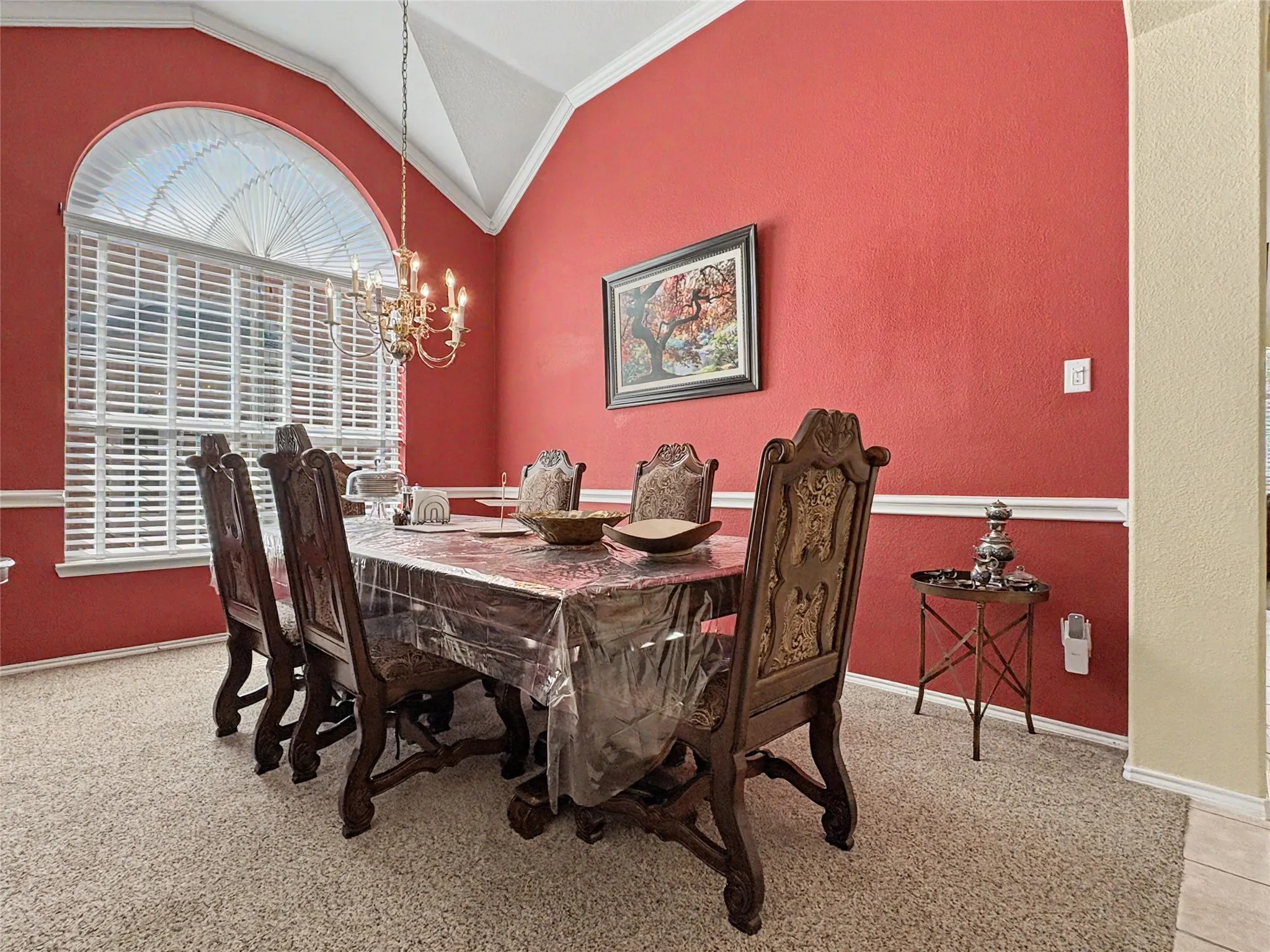 Vaulted ceiling with crown molding, chandelier lighting, arched window with horizontal blinds, red-painted walls with white chair rail molding, and carpet flooring