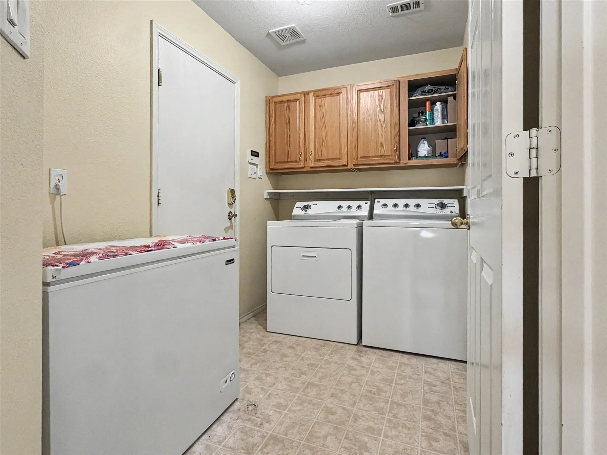Laundry area featuring wood cabinetry, a utility shelf, and tile flooring