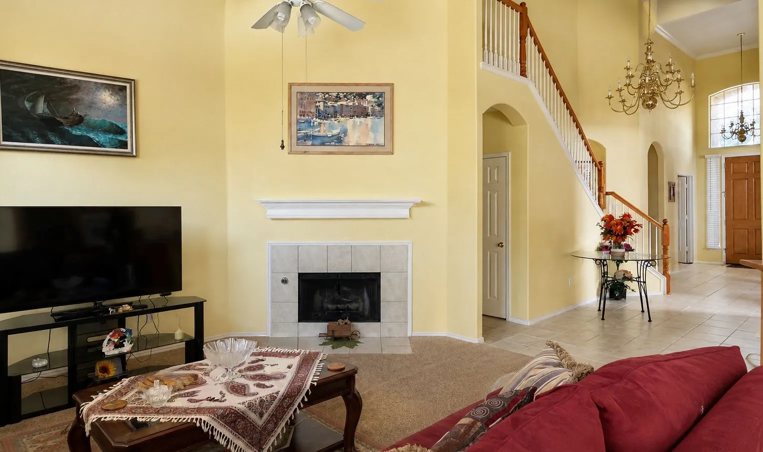 Tile-surround fireplace with a white mantle, wood-railed staircase, high ceilings, and a chandelier