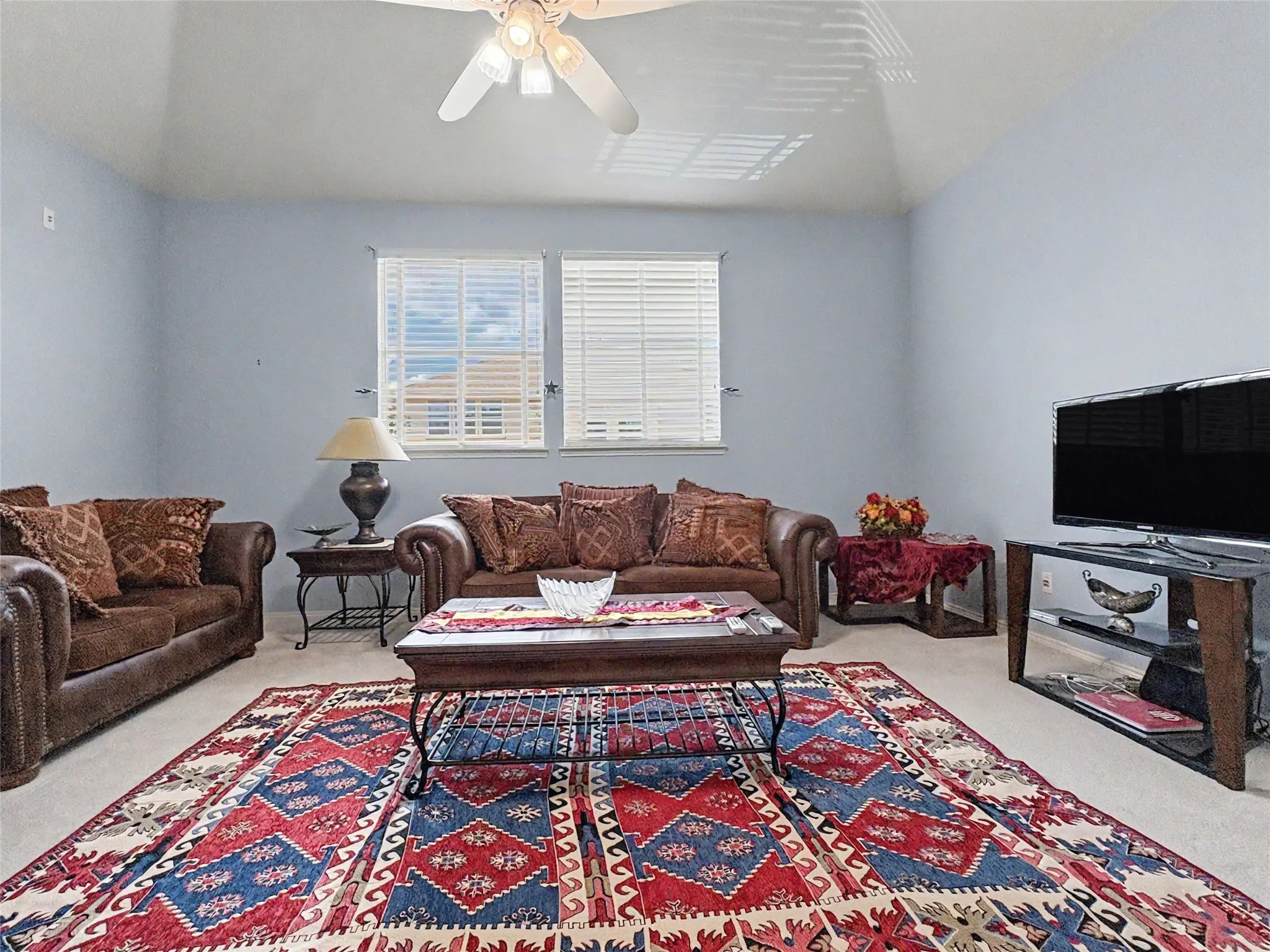 Vaulted ceiling with a ceiling fan light fixture, two windows with blinds, and light-colored wall paint